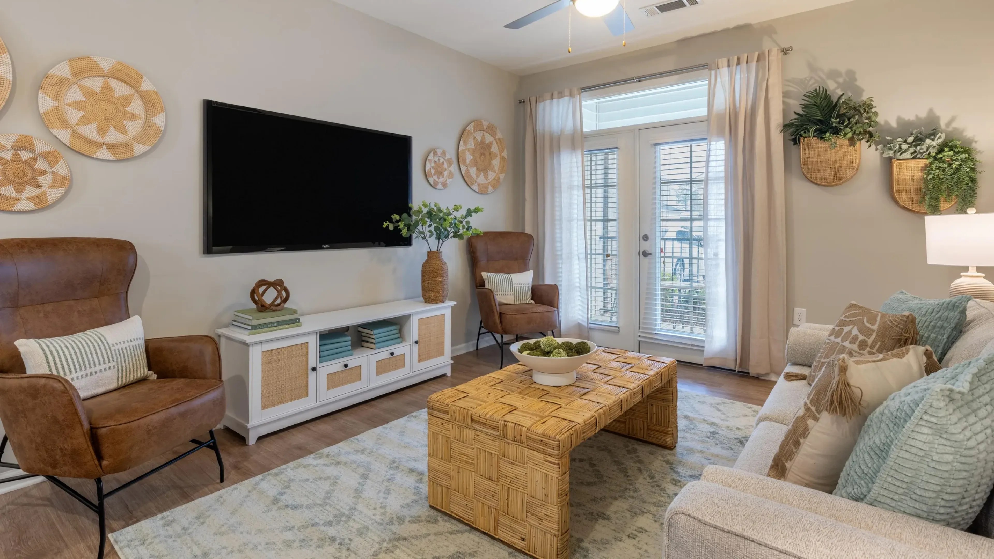 Hawthorne at Leland apartment interior living room, couch, coffee table, rug, chair, TV, ceiling fan, and french doors out to the patio