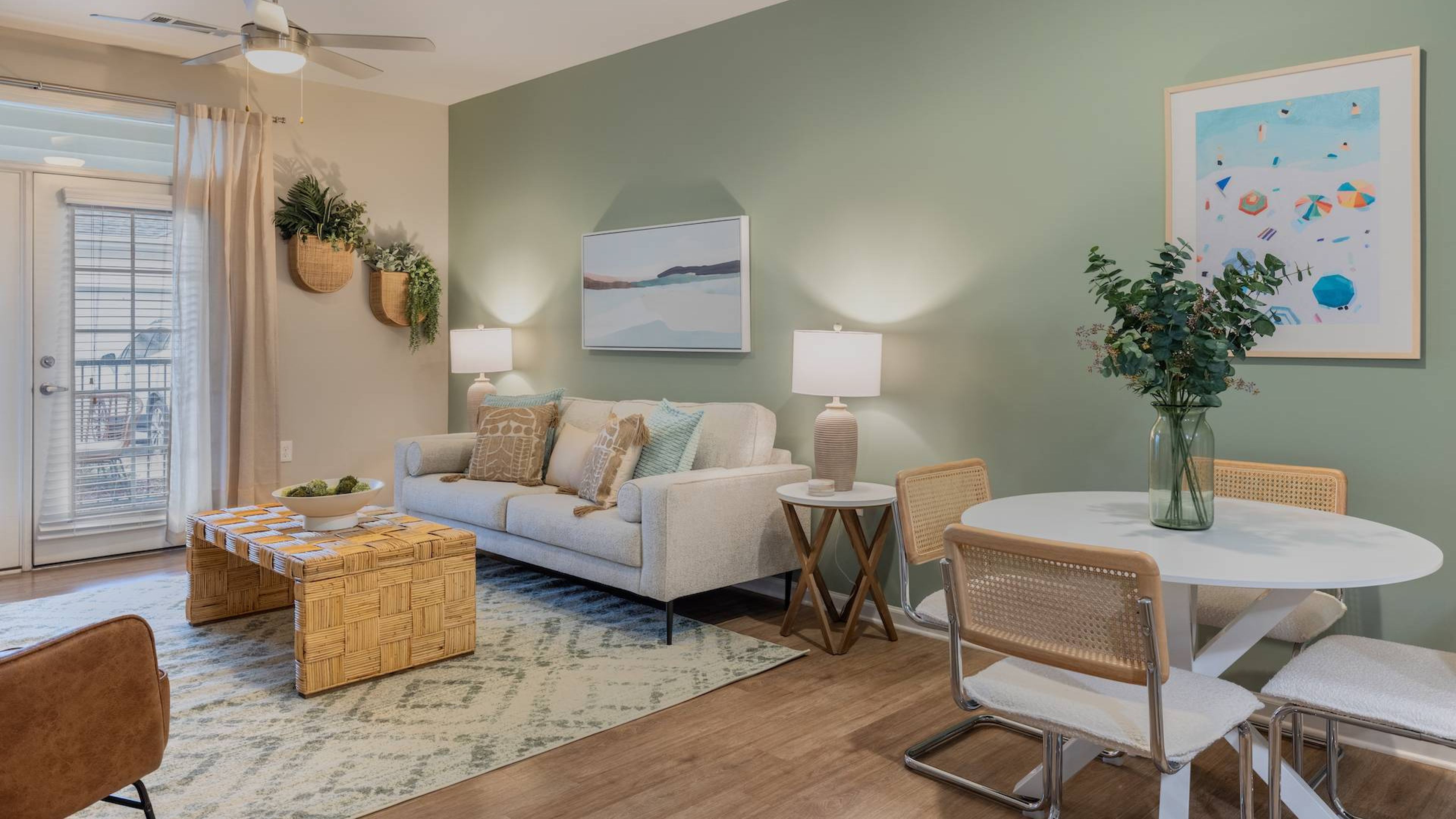 Hawthorne at Leland cozy living room featuring a beige couch, a woven coffee table, and a dining area, decorated with modern art and greenery.