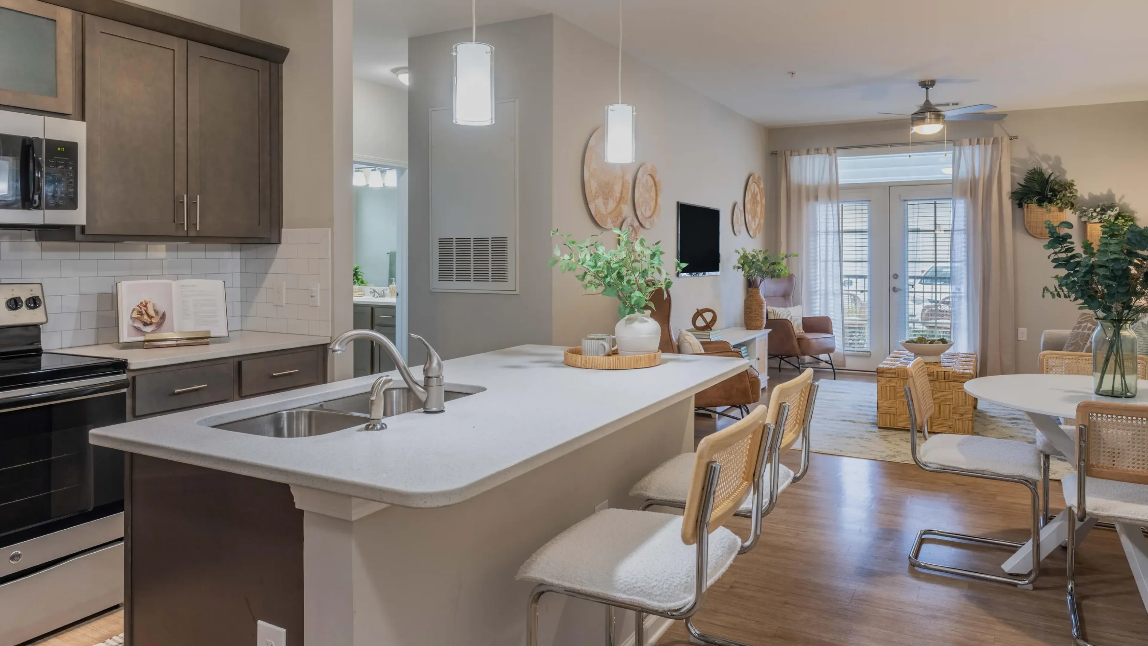 Hawthorne at Leland apartment interior kitchen and living area with kitchen island, bar stools, custom cabinets, living room furniture, and french doors to the patio