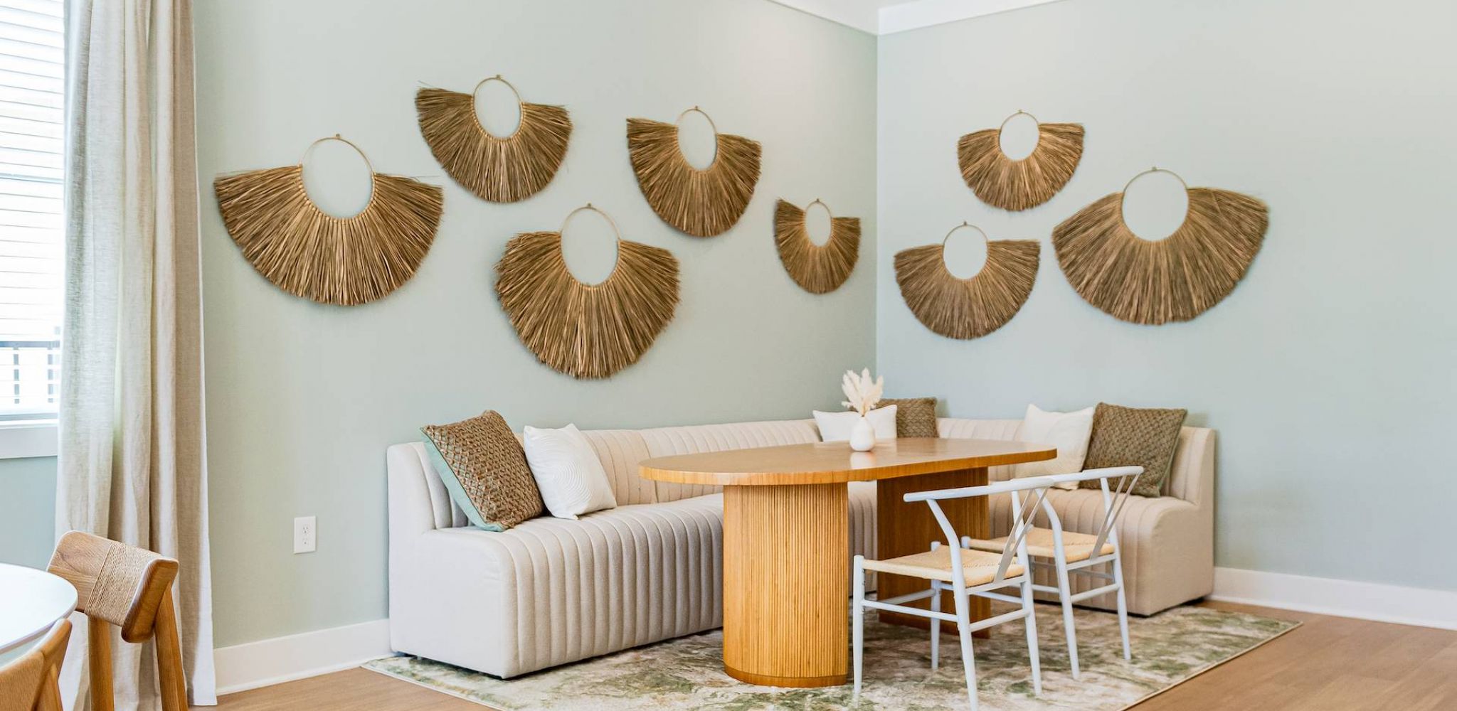 Hawthorne at Leland cozy nook with a white sectional sofa and a wooden dining table beneath decorative woven wall art.
