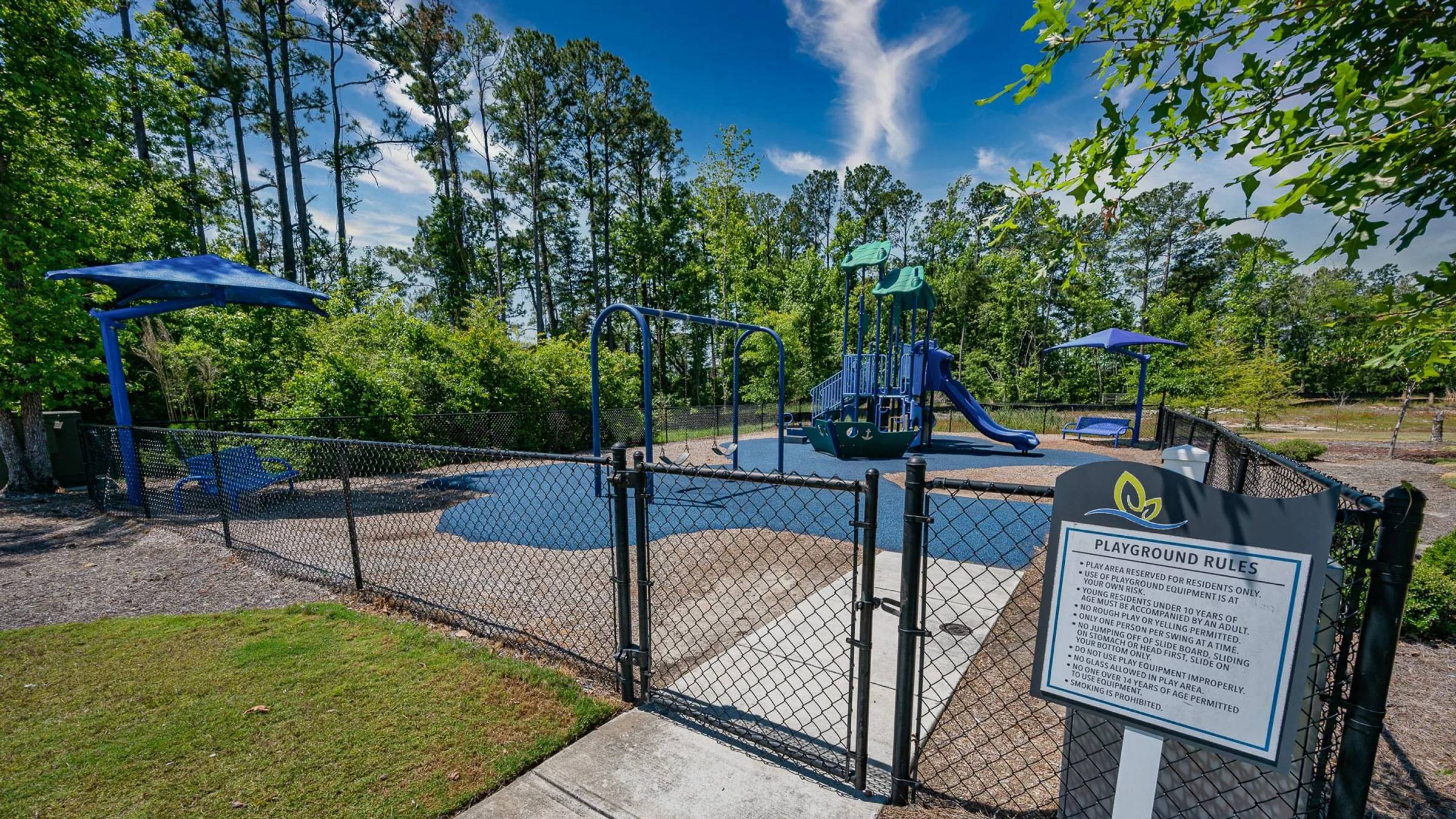 Hawthorne at Leland apartment community large fenced playground surrounded by mature tall green trees and plants